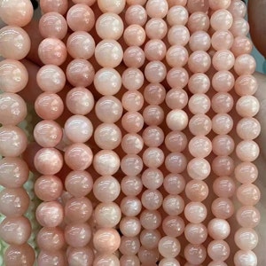 Puede incluir: Primer plano de varios hilos de cuentas de piedras preciosas rosas. Las cuentas son esf&eacute;ricas y tienen una superficie lisa y brillante. El color var&iacute;a de un rosa p&aacute;lido a un rosa m&aacute;s intenso. Las cuentas est&aacute;n ensartadas, ideales para la creaci&oacute;n de joyas.