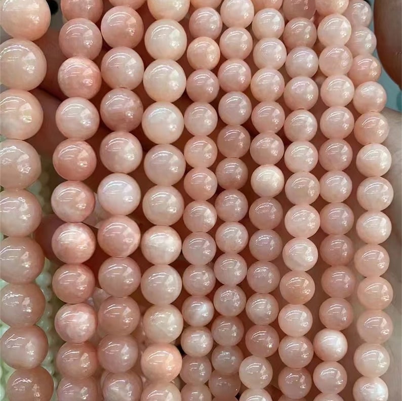 Puede incluir: Primer plano de varios hilos de cuentas de piedras preciosas rosas. Las cuentas son esf&eacute;ricas y tienen una superficie lisa y brillante. El color var&iacute;a de un rosa p&aacute;lido a un rosa m&aacute;s intenso. Las cuentas est&aacute;n ensartadas, ideales para la creaci&oacute;n de joyas.