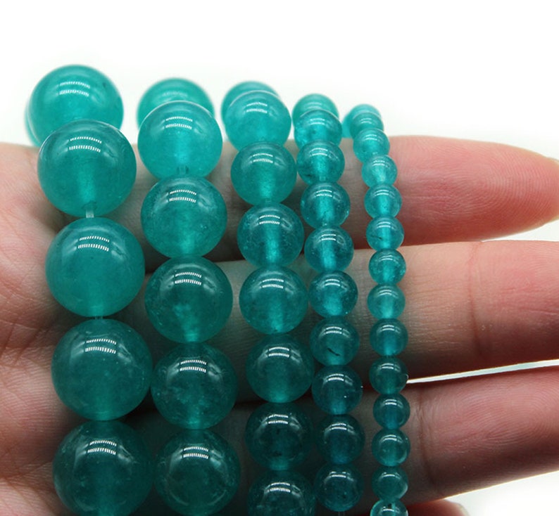 K&ouml;nnte beinhalten: Ein Satz aus vier Str&auml;ngen von tealgr&uuml;nen Edelsteinperlen. Die Perlen sind rund und glatt und auf einer durchsichtigen Gummikordel aufgef&auml;delt.