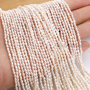 Może przedstawiać: Sznury małych, kremowobiałych, owalnych pereł. Perły są nawleczone, tworząc wiele sznurów. Obraz jest dobrze oświetlony, ukazując naturalny połysk pereł. Tło jest w neutralnym kolorze.