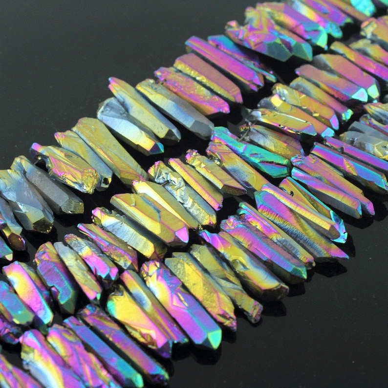 K&ouml;nnte beinhalten: Eine Str&auml;hne aus irisierenden, facettierten Kristallquarzspitzen. Die Spitzen sind in Gold, Lila, Blau und Gr&uuml;n gehalten.