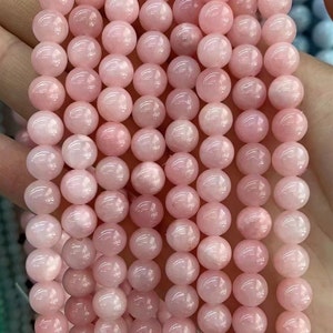 Puede incluir: Un hilo de cuentas redondas de color rosa p&aacute;lido. Las cuentas son de tama&ntilde;o uniforme y tienen una superficie lisa y pulida. El color es un rosa pastel suave, y las cuentas parecen estar ensartadas. La imagen es un primer plano, que destaca los detalles de las cuentas.