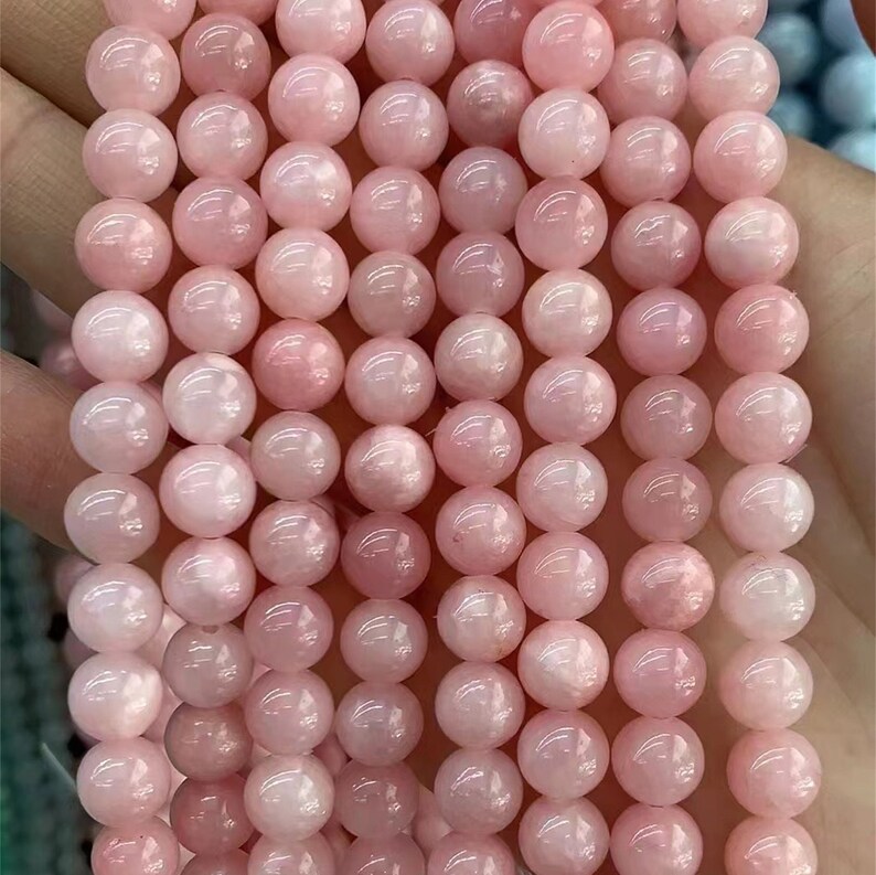 Puede incluir: Un hilo de cuentas redondas de color rosa p&aacute;lido. Las cuentas son de tama&ntilde;o uniforme y tienen una superficie lisa y pulida. El color es un rosa pastel suave, y las cuentas parecen estar ensartadas. La imagen es un primer plano, que destaca los detalles de las cuentas.