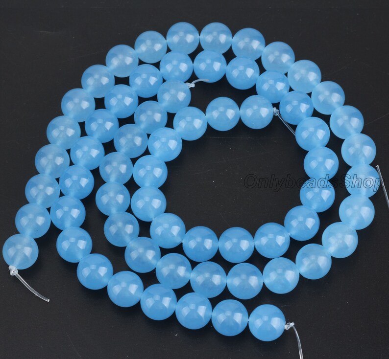 May include: A strand of light blue round gemstone beads. The beads are smooth and polished, and they are strung on a clear thread.