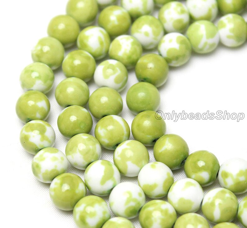May include: A strand of green and white ceramic beads. The beads are round and have a marbled pattern.