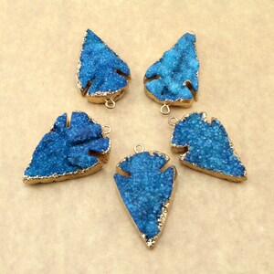 May include: Five blue agate arrowhead pendants with gold-plated edges and jump rings. The arrowheads are all different shapes and sizes.