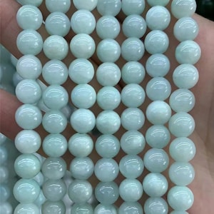 Puede incluir: Un collar de cuentas redondas de piedra preciosa de color azul verdoso p&aacute;lido. Las cuentas son lisas y de tama&ntilde;o uniforme, con un brillo sutil. Las cuentas est&aacute;n ensartadas, listas para la fabricaci&oacute;n de joyas. El color general es un aguamarina suave y apagado.