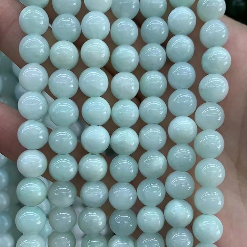 Puede incluir: Un collar de cuentas redondas de piedra preciosa de color azul verdoso p&aacute;lido. Las cuentas son lisas y de tama&ntilde;o uniforme, con un brillo sutil. Las cuentas est&aacute;n ensartadas, listas para la fabricaci&oacute;n de joyas. El color general es un aguamarina suave y apagado.