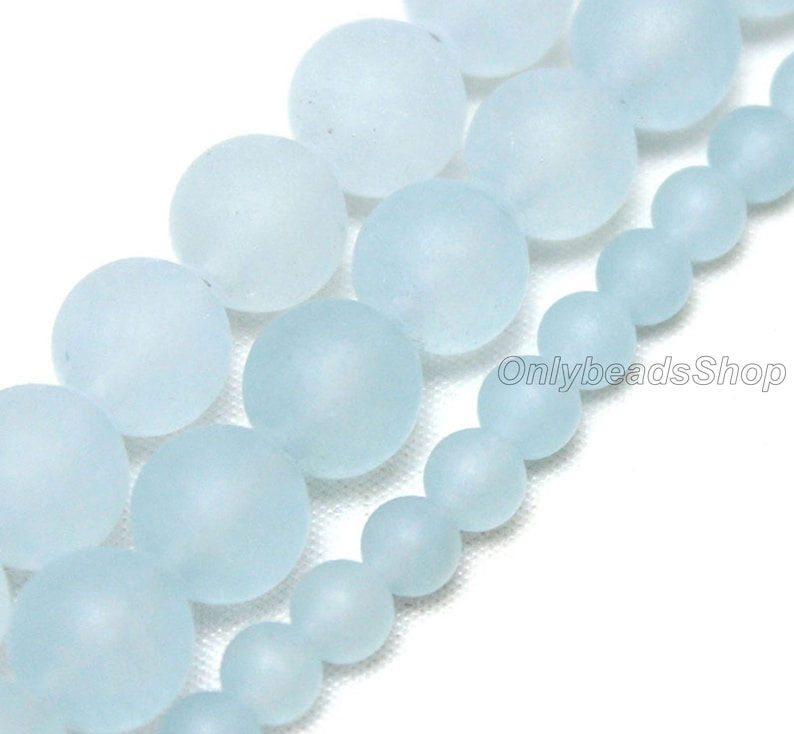 May include: A strand of frosted glass beads in various sizes, ranging from small to large. The beads are a light blue colour and have a smooth, matte finish. The beads are strung together on a clear thread.