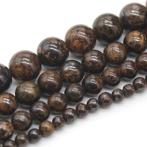 May include: A strand of brown and black gemstone beads. The beads are round and have a speckled appearance. The beads are arranged in a graduated size, with the largest beads at the top and the smallest beads at the bottom.