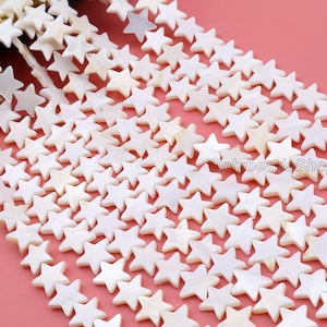 Op de afbeelding: Close-up van strengen witte, stervormige kralen. De kralen hebben een parelmoerglans en zijn aan elkaar geregen. De afbeelding toont de details van de kralen en hun rangschikking. De kralen zijn uniform in grootte en vorm.