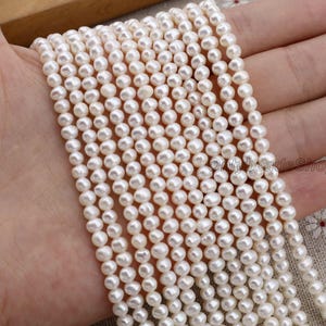 May include: Strands of small, white pearls. The pearls are round and have a smooth, lustrous surface. The pearls are strung together, creating a delicate and elegant look. The image is of a hand holding the strands of pearls.