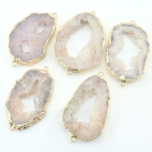 May include: Five white agate slices with gold-toned metal accents. Each slice has a natural, irregular shape with a hole in the centre. The agate is translucent and has a white and pink colour.