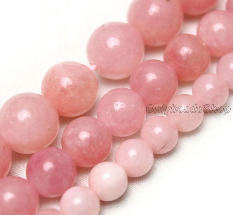 May include: A strand of pink gemstone beads. The beads are round and smooth, with a slight shimmer. The beads are strung on a clear thread.