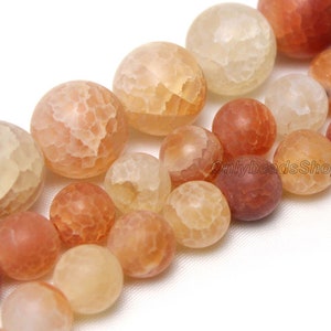May include: A strand of agate beads in various shades of orange and white. The beads are round and have a textured surface.