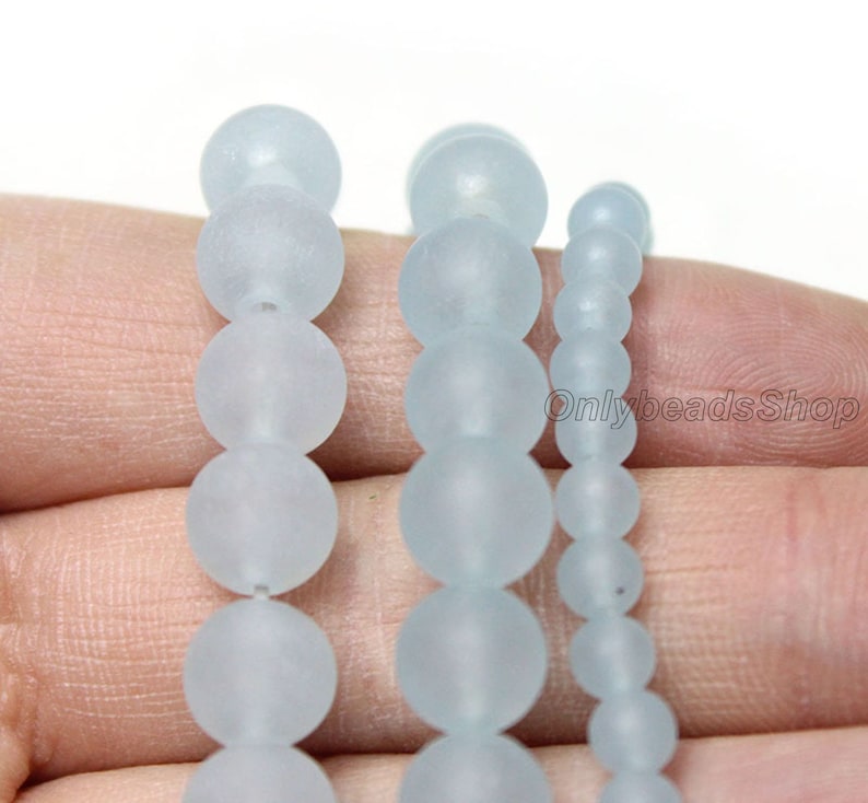 May include: Three strands of frosted glass beads in different sizes. The beads are round and translucent, with a light blue colour.