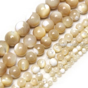 May include: A range of sizes of round, white and beige shell beads with an iridescent sheen. The beads are arranged in rows from largest to smallest.