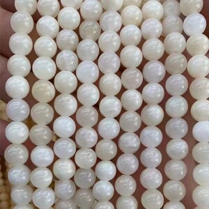 Puede incluir: Hilo de cuentas blancas redondas y luminosas. Las cuentas tienen un brillo nacarado, que refleja la luz. Las cuentas est&aacute;n ensartadas, lo que sugiere que son para la fabricaci&oacute;n de joyas o manualidades. La paleta de colores general es suave y neutra.