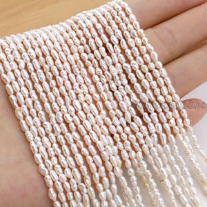 May include: A strand of creamy white, oval-shaped freshwater pearls. The pearls are strung together, creating a flowing, textured appearance. The beads are uniform in size and shape, with a subtle lustre.
