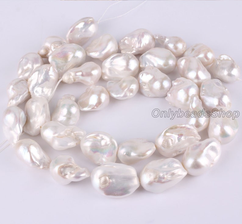 Peut inclure: Un brin de perles baroques blanches, avec un &eacute;clat iridescent. Les perles sont de forme et de taille irr&eacute;guli&egrave;res, et sont enfil&eacute;es sur un fil blanc.