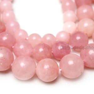 May include: A strand of pink gemstone beads. The beads are round and smooth, with a glossy finish. The beads are strung on a clear thread.