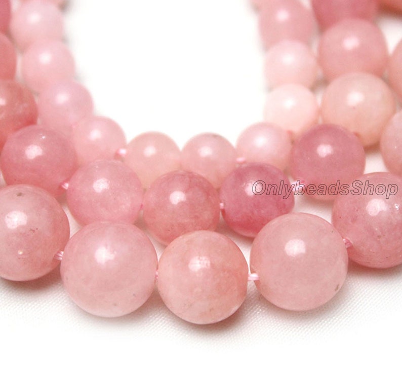 May include: A strand of pink gemstone beads. The beads are round and smooth, with a glossy finish. The beads are strung on a clear thread.