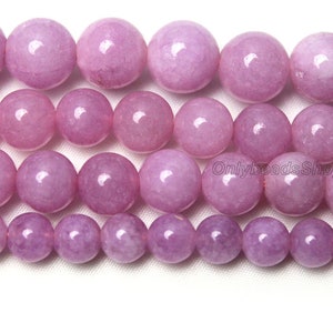 Puede incluir: Una hebra de cuentas redondas de piedras preciosas de color lavanda. Las cuentas son lisas y pulidas, con un ligero brillo. Las cuentas est&aacute;n dispuestas en un patr&oacute;n escalonado, con las cuentas m&aacute;s grandes en el centro y las m&aacute;s peque&ntilde;as en los bordes.