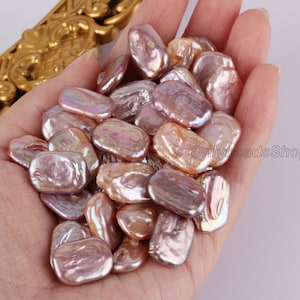 May include: A collection of approximately 30 oval-shaped, iridescent, pink and peach freshwater pearls. The pearls are loose and have a natural, irregular shape.