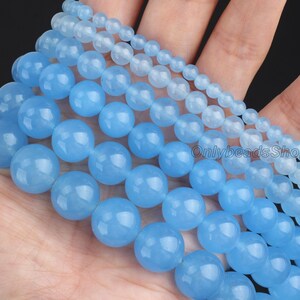 May include: A set of six strands of light blue round gemstone beads. The beads are of varying sizes, with the largest beads being approximately 2.5 cm in diameter. The beads are smooth and polished, and they have a translucent appearance.