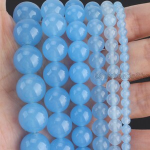 May include: Assortment of light blue round gemstone beads in various sizes. The beads are smooth and polished, with a translucent appearance.