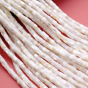 May include: Close-up of strands of white, square-shaped beads. The beads have a slightly iridescent quality and are strung together, creating a textured surface. The beads are likely for jewelry making.