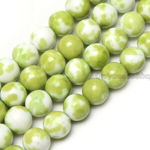 May include: A strand of green and white jade beads. The beads are round and have a mottled pattern. The beads are strung on a clear thread.