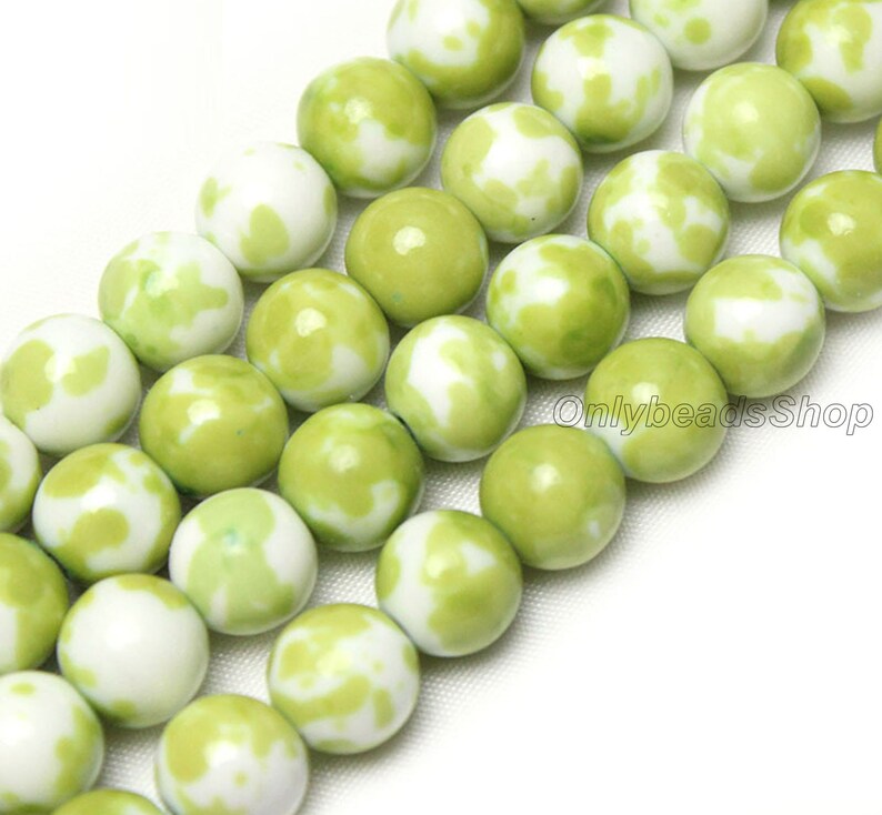 May include: A strand of green and white jade beads. The beads are round and have a mottled pattern. The beads are strung on a clear thread.