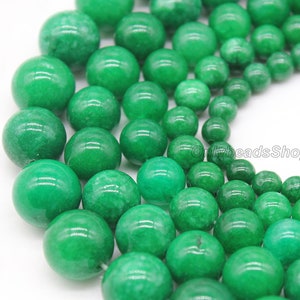 May include: A close-up of a collection of round, green jade beads. The beads are various sizes and are arranged in a random pattern.