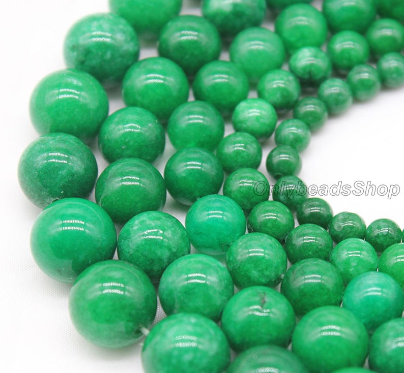 May include: A close-up of a collection of round, green jade beads. The beads are various sizes and are arranged in a random pattern.