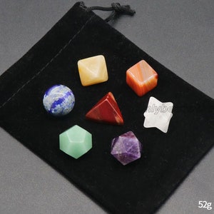 Könnte beinhalten: Sieben pyramidenförmige Edelsteinkristalle in einem schwarzen Samtbeutel. Die Kristalle sind in verschiedenen Formen und Farben, darunter rot, orange, gelb, grün, blau, lila und weiß. Der Beutel hat einen Kordelverschluss und ist mit "52g" beschriftet.