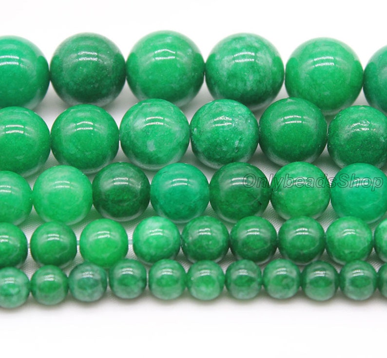 May include: A strand of green jade beads in various sizes. The beads are round and smooth, with a polished finish. The beads are arranged in rows, with the largest beads at the top and the smallest beads at the bottom.