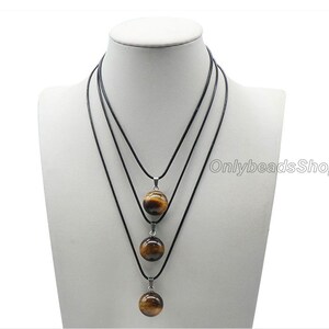 May include: Three layered necklaces with black cords and tiger's eye stone pendants. The pendants are round and graduated in size, with the largest pendant at the bottom.