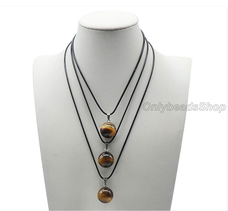 May include: Three layered necklaces with black cords and tiger's eye stone pendants. The pendants are round and graduated in size, with the largest pendant at the bottom.