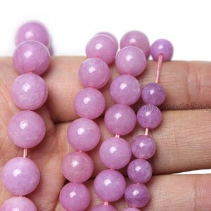 Puede incluir: Una hebra de cuentas redondas de color p&uacute;rpura claro hechas de piedra natural. Las cuentas son lisas y pulidas, con un ligero brillo. Las cuentas est&aacute;n enhebradas en un cord&oacute;n el&aacute;stico delgado y transparente.