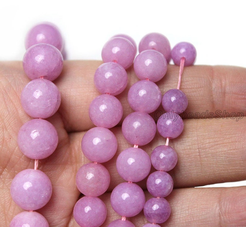 Puede incluir: Una hebra de cuentas redondas de color p&uacute;rpura claro hechas de piedra natural. Las cuentas son lisas y pulidas, con un ligero brillo. Las cuentas est&aacute;n enhebradas en un cord&oacute;n el&aacute;stico delgado y transparente.