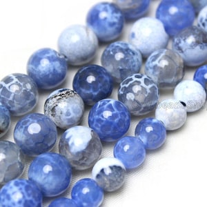 May include: A strand of blue agate beads with white and grey patterns. The beads are round and smooth, and they are strung on a clear thread.