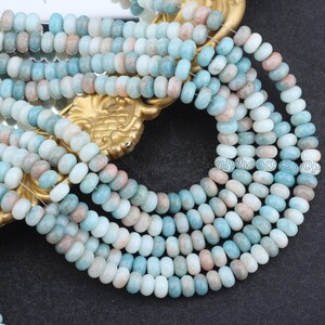 Pu&ograve; includere: Primo piano di fili di perline di pietre preziose nei toni del blu, bianco e pesca. Le piccole perline rotonde hanno una forma leggermente irregolare. Infilate insieme, i fili sono disposti in modo decorativo. Queste perline sono probabilmente destinate alla creazione di gioielli.