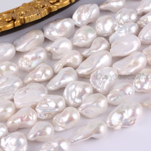 Peut inclure: Un brin de perles baroques blanches, avec un &eacute;clat iridescent. Les perles sont de forme et de taille irr&eacute;guli&egrave;res, et sont enfil&eacute;es sur un fil transparent. Les perles sont pr&eacute;sent&eacute;es sur un fond blanc.
