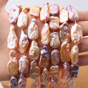 Puede incluir: Primer plano de hilos de perlas barrocas de agua dulce. Las perlas son de tonos melocotón, rosa y lavanda, con un brillo iridiscente. Tienen una forma irregular y están ensartadas. La imagen destaca la belleza natural y las formas únicas de las perlas.