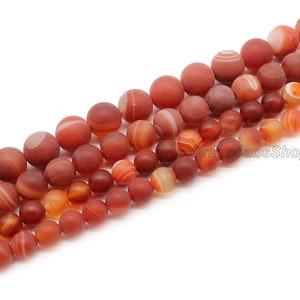 May include: A strand of red agate beads with white and orange stripes. The beads are round and smooth, and they are arranged in a line.
