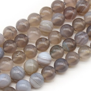 May include: A strand of grey agate beads with white and grey banding. The beads are round and smooth, and they are strung on a clear thread.