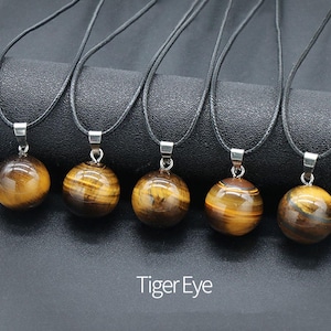May include: Five necklaces with black cords and round tiger's eye stone pendants. The pendants are all the same size and shape, and they have a golden brown color with a slight shimmer.