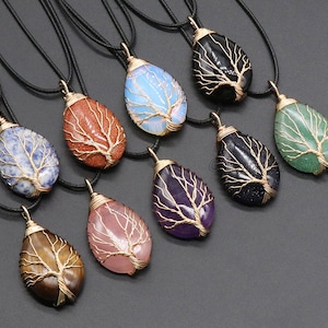 Puede incluir: Un conjunto de diez collares con colgantes de árbol de la vida envueltos en alambre. Cada colgante está hecho con un tipo diferente de piedra preciosa, incluyendo amatista, cuarzo rosa, ojo de tigre y aventurina.