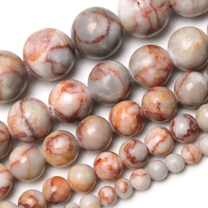 May include: A strand of round, white and brown agate beads with red and brown marbling. The beads are various sizes and are strung on a clear thread.